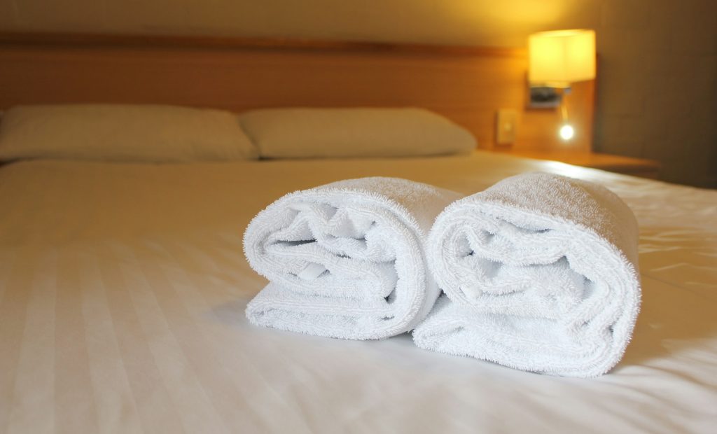 Bedside lamp, pillows and hotel room bed with fresh towels laid out