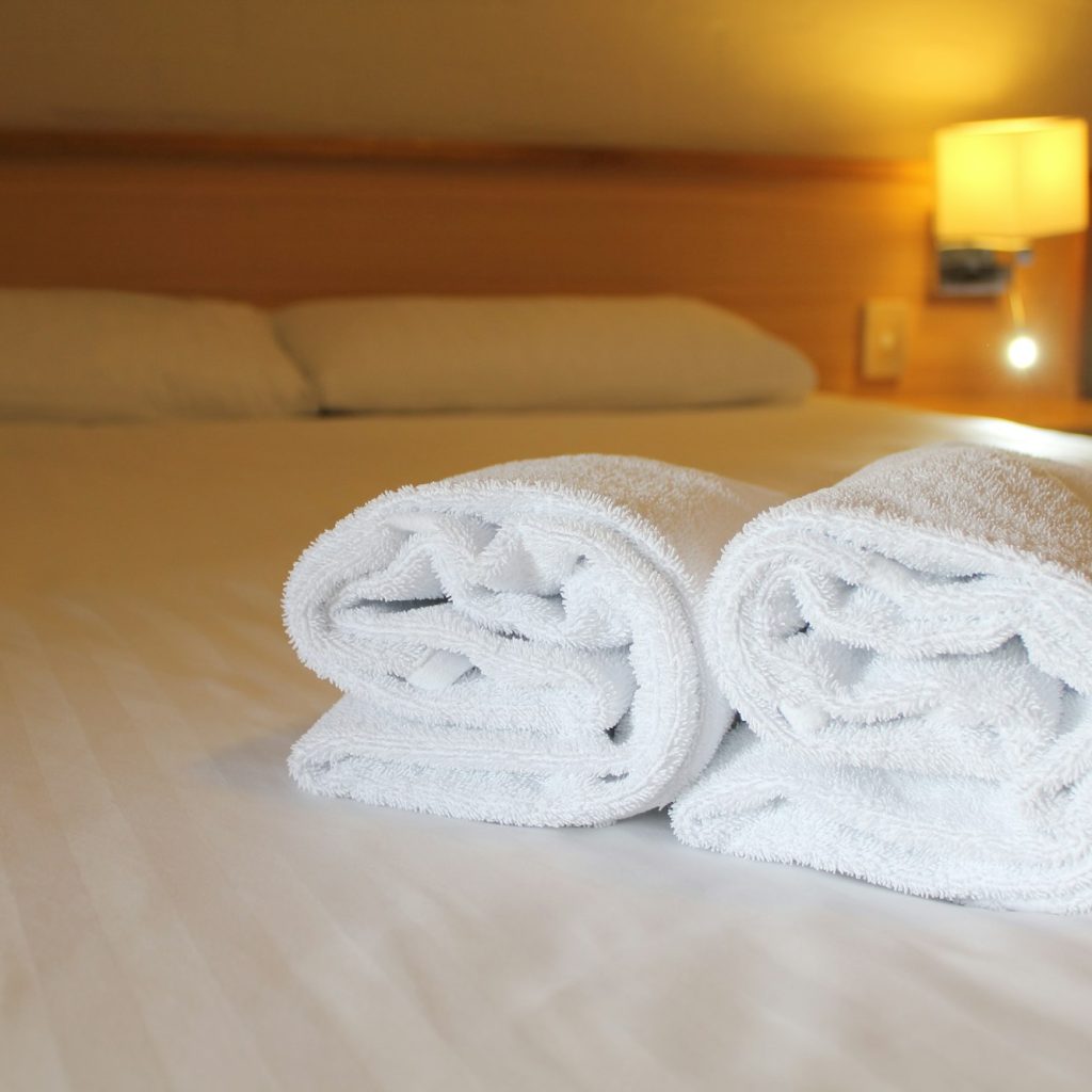 Bedside lamp, pillows and hotel room bed with fresh towels laid out