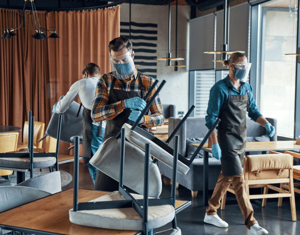 Male waiters in protective workwear arranging furniture in restaurant