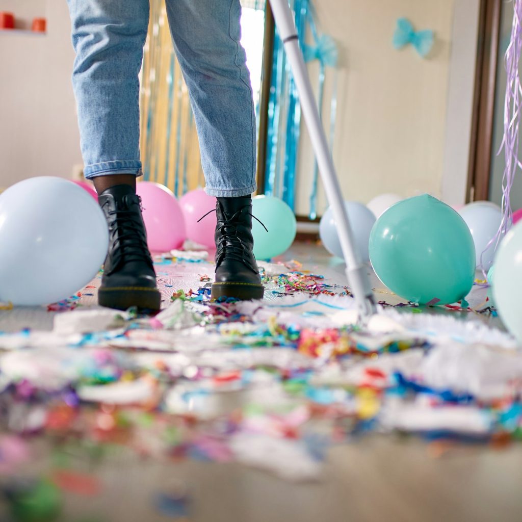 Woman with pushbroom cleaning mess of floor in room after party confetti